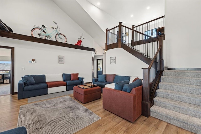 living area with stairway, recessed lighting, light wood-style floors, and a towering ceiling