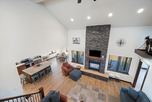 living area featuring a stone fireplace, recessed lighting, wood finished floors, and high vaulted ceiling