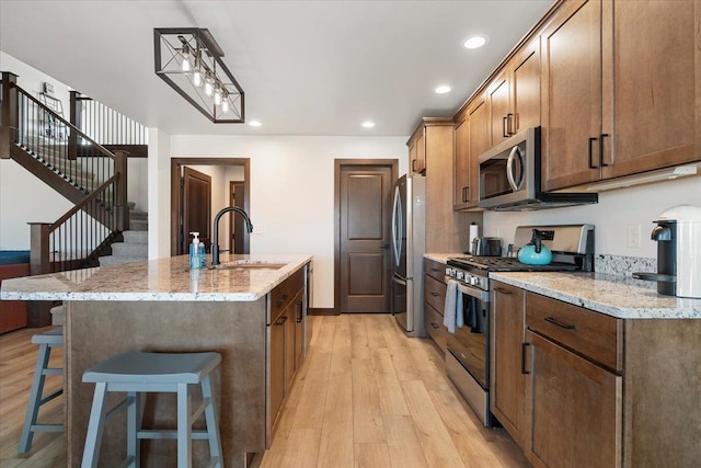 kitchen with a sink, a kitchen bar, light wood-type flooring, appliances with stainless steel finishes, and a kitchen island with sink