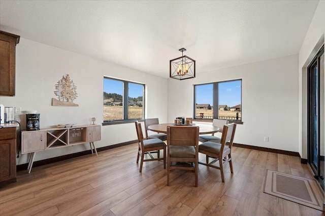 dining space featuring light wood-type flooring, baseboards, and a notable chandelier