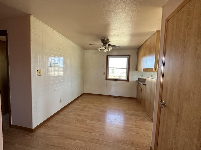 spare room featuring a textured ceiling, baseboards, light wood finished floors, and ceiling fan