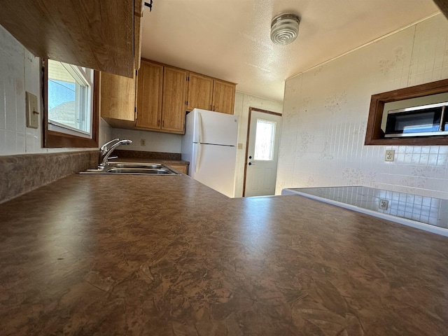 kitchen with dark countertops, freestanding refrigerator, a sink, stainless steel microwave, and a wealth of natural light