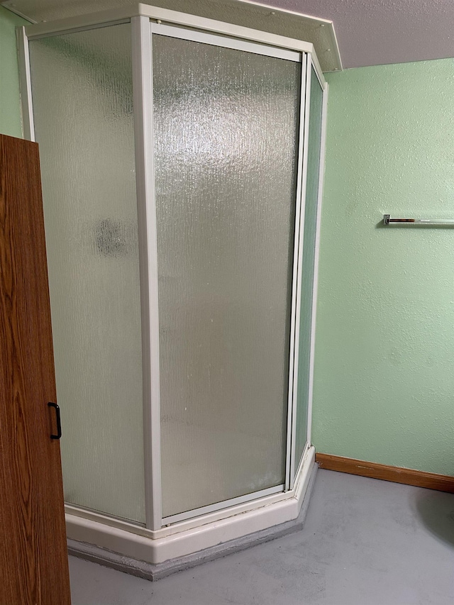 bathroom featuring baseboards, concrete flooring, a shower stall, and a textured wall