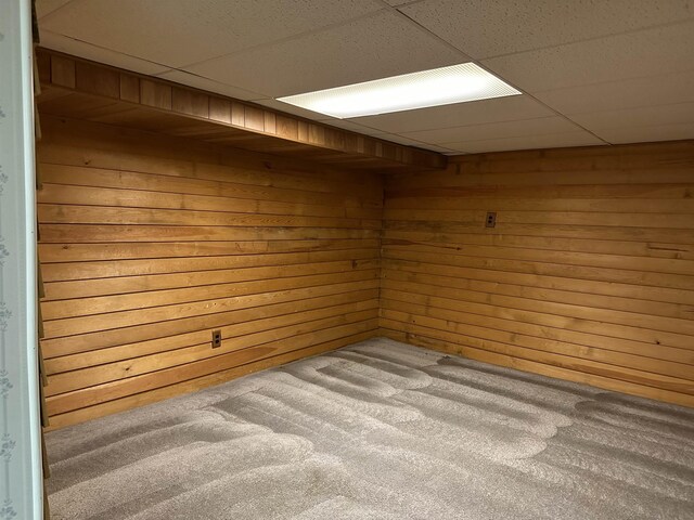 carpeted spare room with a paneled ceiling and wood walls