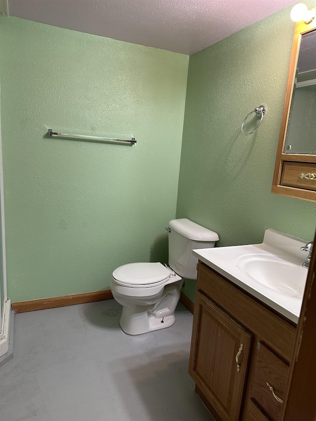 bathroom featuring vanity, toilet, a textured wall, and baseboards