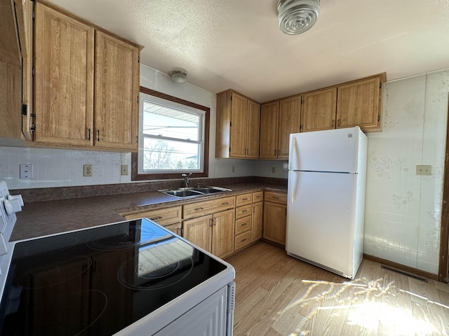 kitchen with a sink, dark countertops, white appliances, light wood-style floors, and brown cabinetry