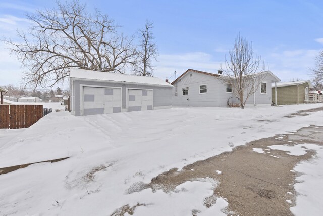 snow covered rear of property featuring a garage, an outdoor structure, and fence