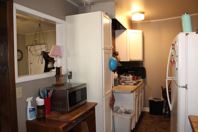 kitchen with a sink, stainless steel microwave, white cabinetry, and freestanding refrigerator