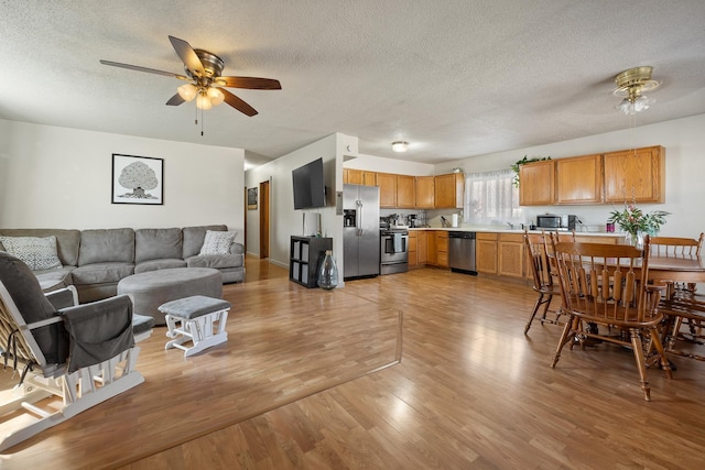 living room with a textured ceiling, light wood-type flooring, and a ceiling fan