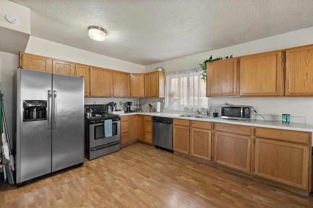 kitchen featuring light countertops, a sink, appliances with stainless steel finishes, brown cabinets, and light wood-style flooring