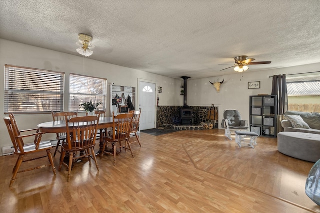 dining room with a wood stove, a textured ceiling, light wood finished floors, ceiling fan, and a baseboard radiator