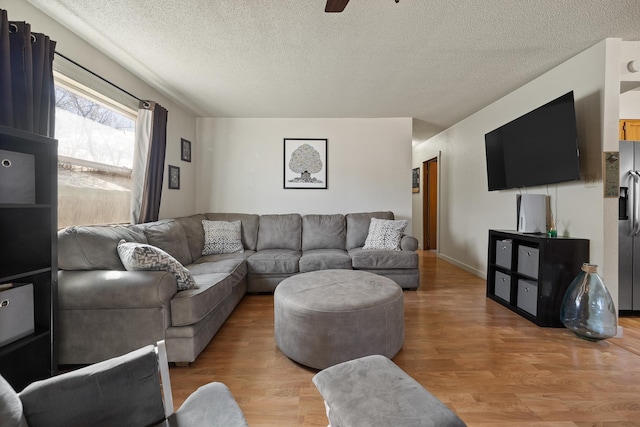 living room with baseboards, a textured ceiling, light wood-style floors, and a ceiling fan