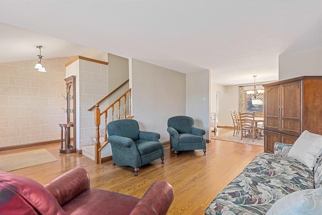 living room featuring stairway, a chandelier, light wood finished floors, a textured ceiling, and lofted ceiling