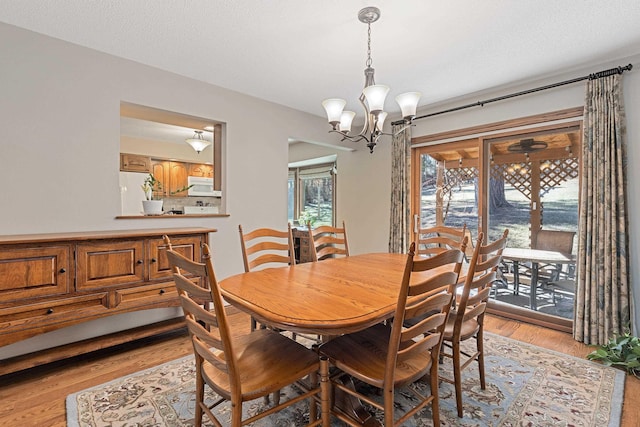 dining room featuring a textured ceiling, an inviting chandelier, and light wood-style floors