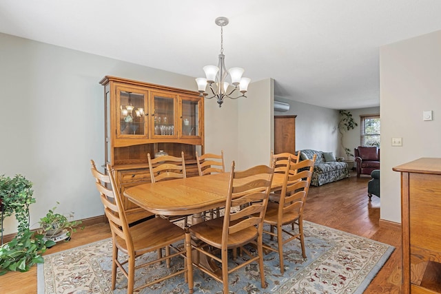 dining area featuring a wall unit AC, a notable chandelier, baseboards, and wood finished floors