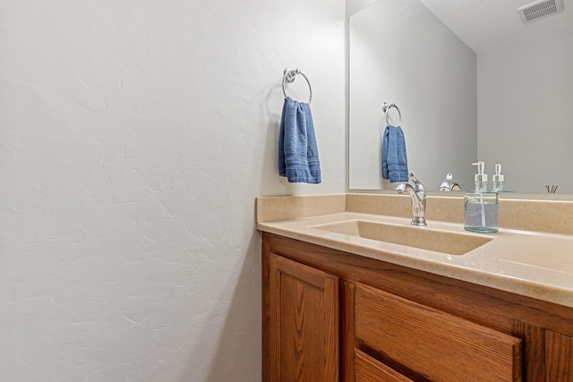 bathroom with vanity, a textured wall, and visible vents