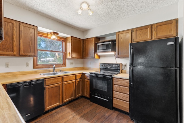 kitchen featuring light countertops, brown cabinets, a sink, dark wood-style floors, and black appliances