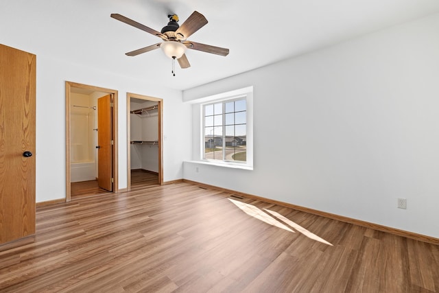 unfurnished bedroom featuring baseboards, a closet, light wood-style flooring, and a spacious closet