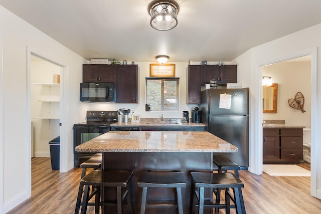 kitchen featuring a sink, a breakfast bar, light wood-style flooring, black appliances, and dark brown cabinets