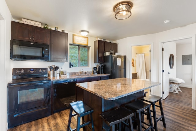 kitchen with electric panel, a kitchen bar, dark brown cabinetry, a sink, and black appliances