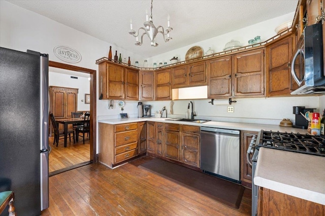 kitchen with dark wood-style flooring, light countertops, brown cabinetry, stainless steel appliances, and a sink
