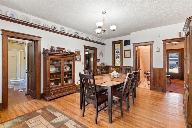 dining area featuring a chandelier, a textured ceiling, wainscoting, and light wood-style flooring