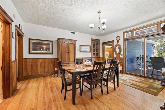 dining space with a chandelier, light wood-type flooring, wainscoting, and a textured ceiling