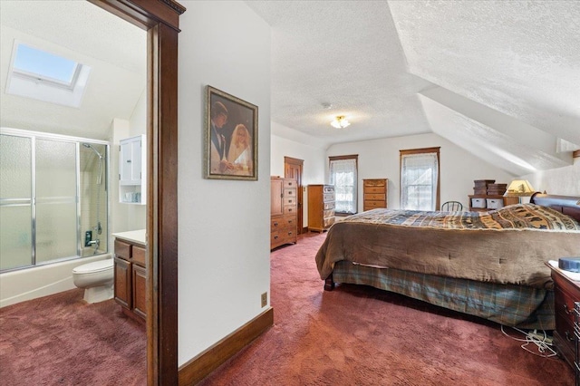 bedroom with ensuite bathroom, dark carpet, a textured ceiling, baseboards, and lofted ceiling with skylight