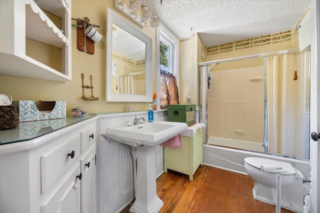 full bathroom featuring a textured ceiling, a sink, enclosed tub / shower combo, and wood finished floors