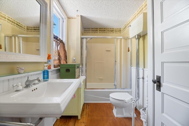 full bathroom with toilet, shower / bath combination with glass door, wood finished floors, and a textured ceiling