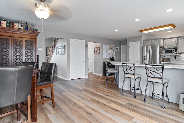 kitchen with light wood finished floors, stainless steel appliances, light countertops, gray cabinets, and a kitchen bar