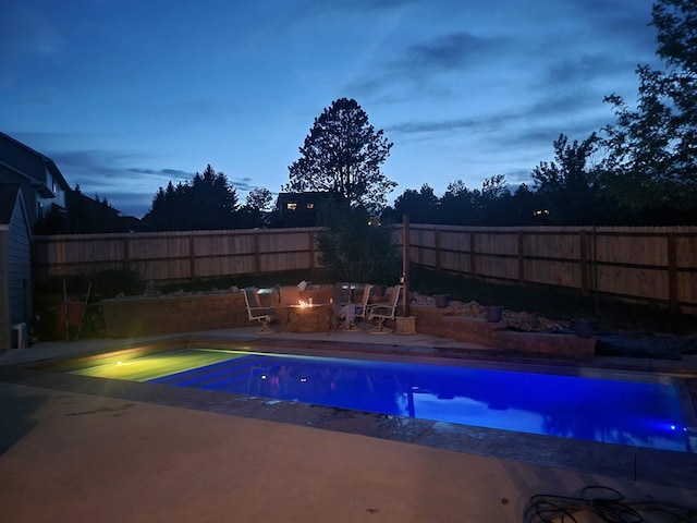 pool at dusk with a fenced in pool, a fenced backyard, a patio, and an outdoor fire pit