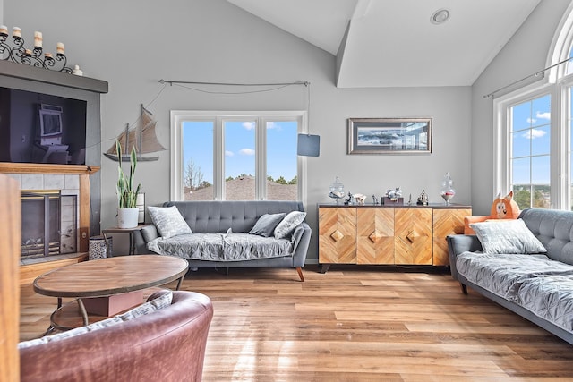 living room with high vaulted ceiling, a tile fireplace, and light wood-style flooring