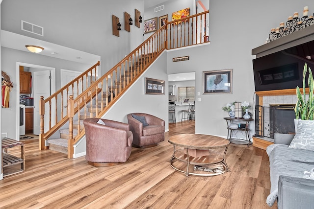 living area with a tiled fireplace, wood finished floors, visible vents, and stairs