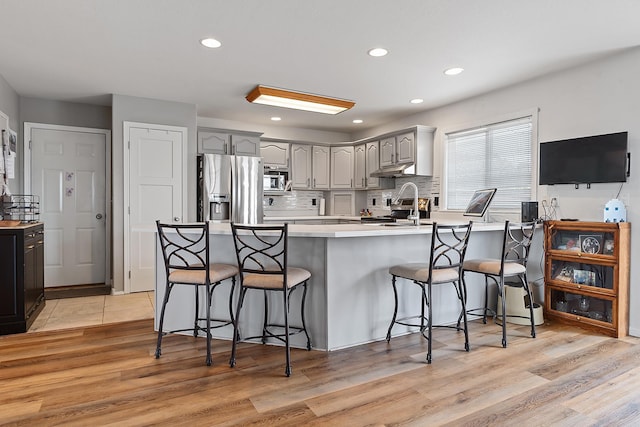 kitchen featuring decorative backsplash, stainless steel appliances, a kitchen bar, a peninsula, and gray cabinetry