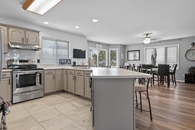 kitchen featuring under cabinet range hood, electric stove, gray cabinets, a peninsula, and a breakfast bar area
