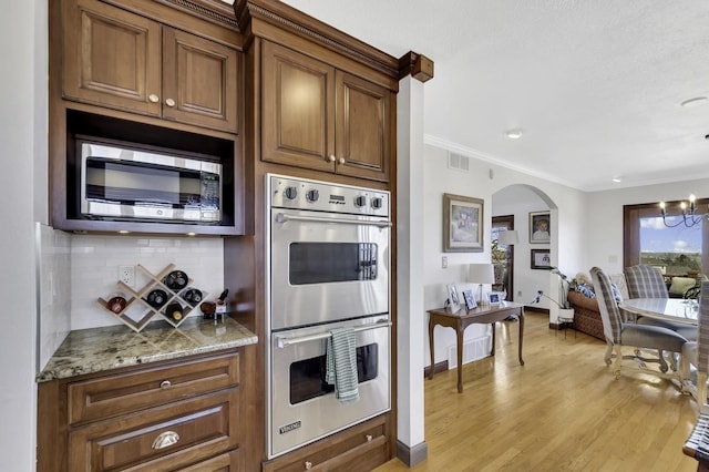 kitchen featuring crown molding, light wood-style flooring, arched walkways, tasteful backsplash, and stainless steel appliances