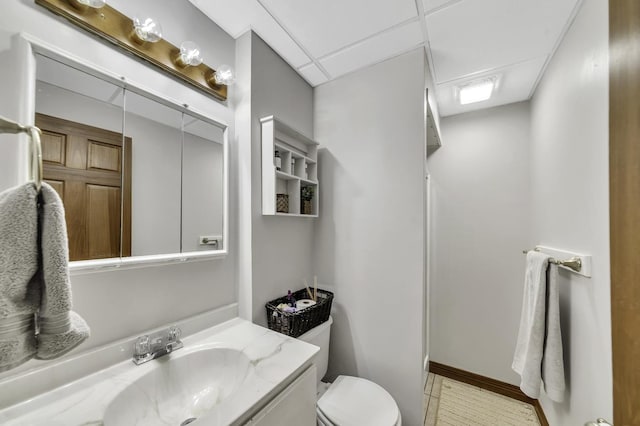 bathroom with toilet, a paneled ceiling, vanity, and baseboards