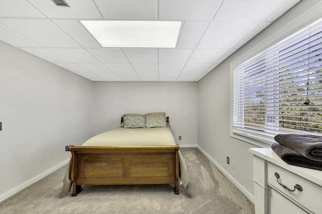 bedroom featuring baseboards, a drop ceiling, and light colored carpet