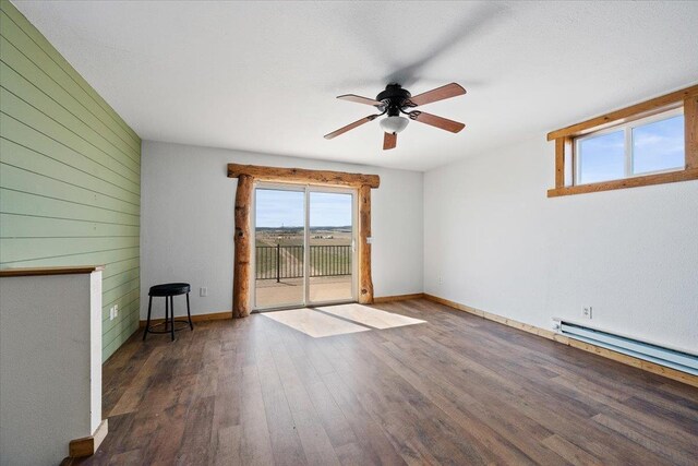 spare room with baseboards, a baseboard heating unit, wooden walls, ceiling fan, and wood finished floors