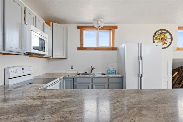 kitchen featuring a sink, white appliances, gray cabinetry, and an inviting chandelier