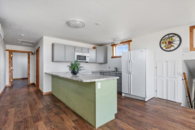 kitchen featuring white appliances, a peninsula, gray cabinetry, dark wood finished floors, and a sink