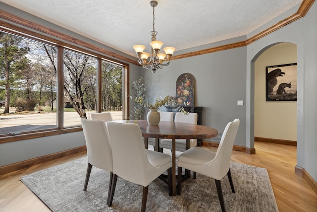 2724 Diamond Oak Pl, Rapid City, SD 57702 - dining area featuring a notable chandelier, baseboards, a textured ceiling, light wood-style floors, and arched walkways
