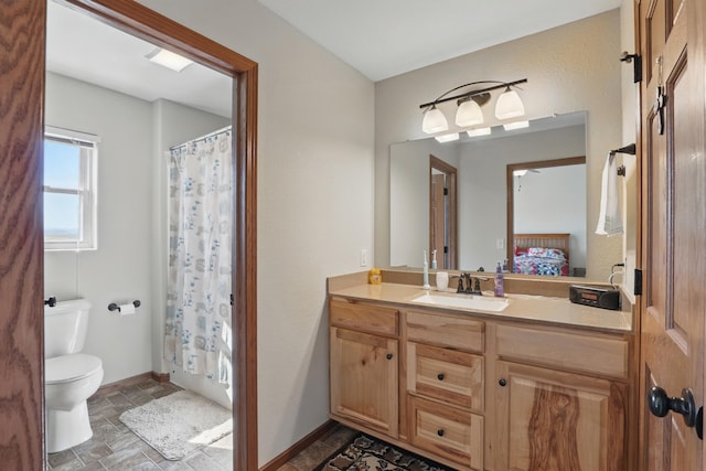 bathroom with ensuite bathroom, vanity, baseboards, stone finish flooring, and toilet