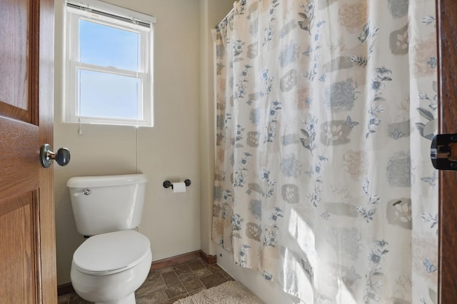 bathroom with baseboards, stone tile flooring, and toilet