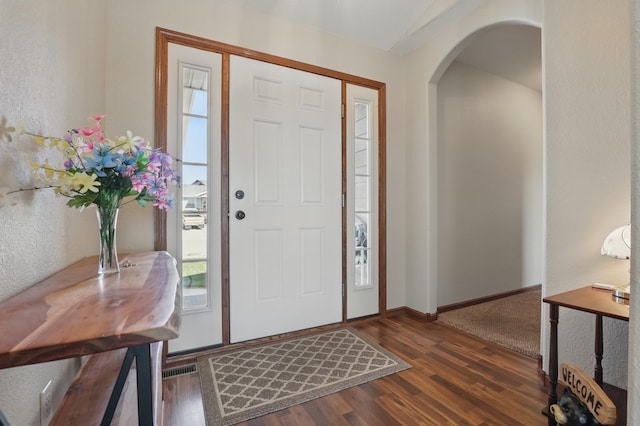 foyer entrance with arched walkways, a healthy amount of sunlight, wood finished floors, and baseboards