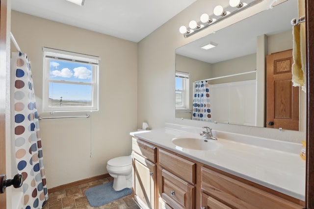 full bathroom featuring curtained shower, stone finish floor, toilet, vanity, and baseboards