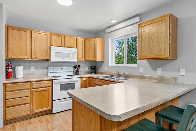 12634 Robins Roost Rd, Hill City, SD 57745 - kitchen featuring a sink, white appliances, light wood-type flooring, a breakfast bar area, and a peninsula