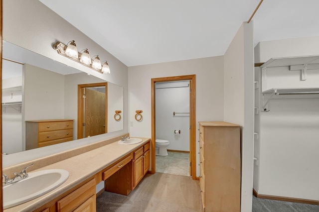 full bathroom with a spacious closet, toilet, a sink, and double vanity