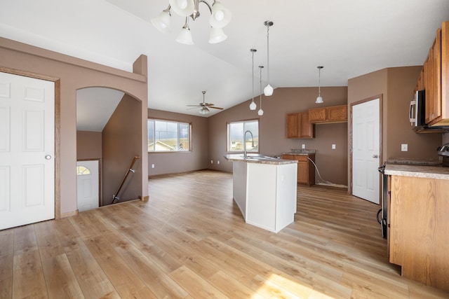 kitchen featuring vaulted ceiling, a sink, stainless steel microwave, light wood-style floors, and brown cabinetry